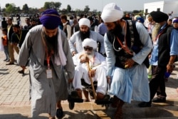 Indian Sikh pilgrims help a man on a wheelchair as they visit the Gurdwara Darbar Sahib, in Kartarpur, Pakistan, Nov. 9, 2019.