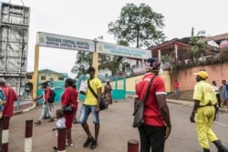 FILE - People wear masks to protect against the COVID-19 coronavirus as they walk by the entrance to the Yaounde General Hospital in Yaounde, March 6, 2020.