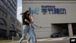 In this Aug. 7, 2020, file photo, women wearing masks to prevent the spread of the coronavirus chat as they pass by the headquarters of ByteDance, owners of TikTok, in Beijing, China. 