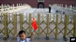 A child holds up a Chinese national flag as he poses for a photo in front of Tiananmen Gate in Beijing, June 4, 2014.
