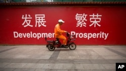 在北京市中心的一條街道上，一名維修工人騎著摩托車經過用中英文書寫的“發展”和“繁榮”的標語（2015年7月15日）。