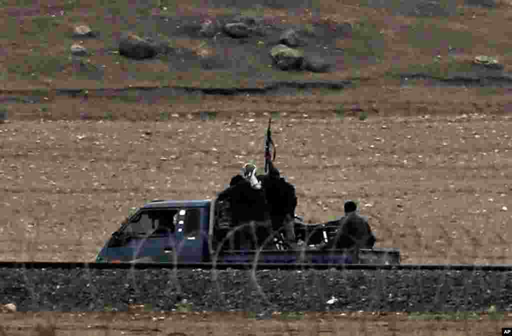 In this image shot with an extreme telephoto lens from the outskirts of Suruc on the Turkey-Syria border, Kurdish fighters with The People’s Protection Units, or YPG, the main Kurdish militia in Syria, patrol in a truck along the border road on the outskirts of western Kobani, Syria, during fighting between Syrian Kurds and the militants of Islamic State group, Oct. 17, 2014.
