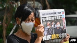 A supporter of two executives from Hong Kong's pro-democracy Apple Daily newspaper, chief editor Ryan Law and CEO Cheung Kim-hung, holds up a copy of the paper during a protest outside court on June 19, 2021, after the two were charged with collision.