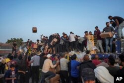 Warga Palestina menyerbu truk berisi bantuan kemanusiaan yang dibawa melalui dermaga baru yang dibangun AS, di Jalur Gaza tengah, Sabtu, 18 Mei 2024. (Foto: AP)