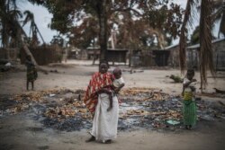 FILE - A woman holds her child while standing in a burned out area in the attacked village of Aldeia da Paz outside Macomia in Cabo Delgado province, in Mozambique, Aug. 24, 2019.