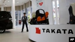 FILE - a security guard stands by child seats, manufactured and displayed by Takata Corp. at an automaker's showroom in Tokyo. Japanese automaker Honda Motor Co. expanded its recalls related to defective air bags.