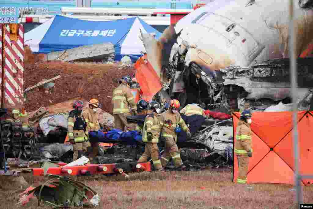 Firefighters carry the body of a passenger from the wreckage of an aircraft that crashed after it went off the runway at Muan International Airport in Muan, South Korea, Dec. 29, 2024. At least 179 people died when the Jeju Air jet belly-landed and skidded off the end of the runway, erupting in a fireball as it slammed into a wall at the ariport. Two people, both crew members, were pulled out of the wreckage alive. The plane, carrying 181 people, was returning from Bangkok. 