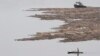 FILE - A North Korean man rows a boat past logs, which were tied together and transported by boats on the Yalu River near the North Korean city of Hyesan, Aug. 16, 2014.