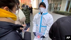 2022年1月26日(週三)，一名身穿防護服的工作人員手持印有“北京健康碼”的二維碼的紙，在北京一傢私人冠狀病毒檢測中心進行檢測。