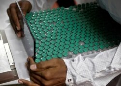 FILE - An employee in personal protective equipment (PPE) removes vials of AstraZeneca's COVISHIELD, coronavirus disease (COVID-19) vaccine from a visual inspection machine inside a lab at Serum Institute of India, in Pune, India, Nov. 30, 2020.