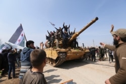 Syrians climb on a Turkish tank in Neyrab, March 15, 2020, as they protest agreement on joint Turkish and Russian patrols in northwest Syria.