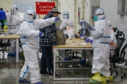 Medical workers in protective suits receive a patient at the Wuhan International Conference and Exhibition Center, which was converted into a makeshift hospital to receive patients with mild symptoms of the coronavirus, in Wuhan, Feb. 5, 2020.