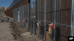 FILE - Workers continue work raising a taller fence on the Mexico-U.S. border separating the towns of Anapra, Mexico, and Sunland Park, New Mexico, Jan. 25, 2017. 