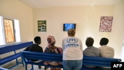 Seorang petugas UNHCR (tengah) berbicara dengan para pengungsi sembari menonton televisi di ruang tunggu kantor UNHCR di Niamey, Niger, 17 November 2017. Para pengungsi dievakuasi dari Libya. 