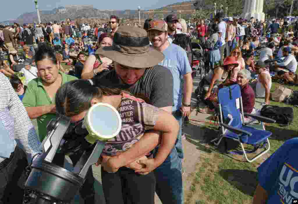 Kayley Terrez is lifted up to see the solar eclipse through a telescope as a large crowd gathers at the Griffith Observatory to watch the solar eclipse in Los Angeles, California, Aug. 21, 2017.