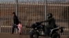 FILE – A migrant and her daughter walk along a secondary border fence in San Ysidro, California, after turning themselves in to U.S. border patrol agents after crossing the border wall from Playas de Tijuana, Mexico, Dec. 4, 2018. 