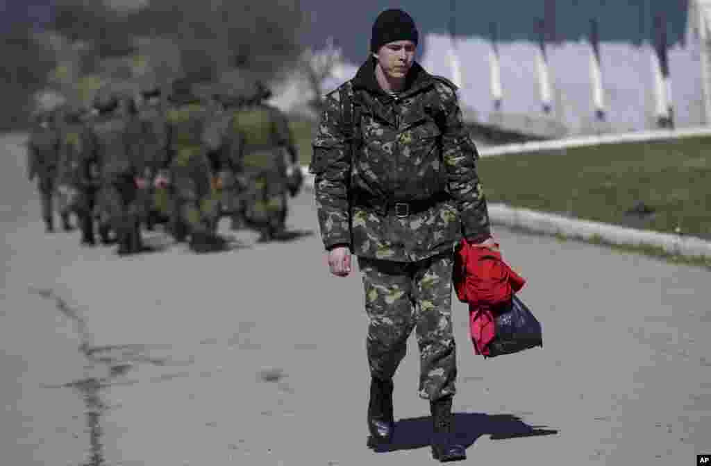 Seorang tentara Ukraina berjalan melewati tentara Rusia yang tengah berbaris menuju barak mereka di luar markas militer di Perevalne, Krimea, 21 Maret 2014.