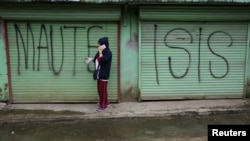 Seorang pria terlihat menggunakan ponsel saat melewati bagian depan toko yang tertutup dengan grafiti "MAUTE-ISIS", di kota Marawi, Filipina selatan, 20 Oktober 2017. (Foto: Reuters)
