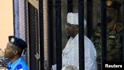 FILE - Sudan's former president Omar Hassan al-Bashir stands guarded inside a cage at the courthouse where he is facing corruption charges, in Khartoum, Sudan, Aug. 19, 2019.